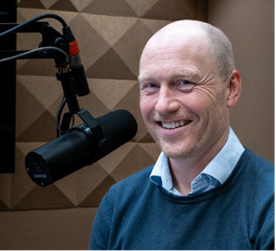 En mann som smiler med et kamera på skulderen