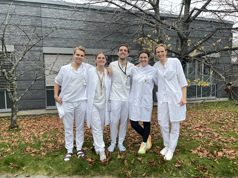 En gruppe mennesker iført hvite laboratoriefrakker som står foran et hus