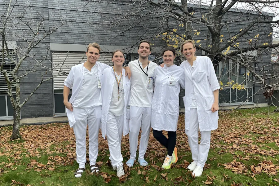 En gruppe mennesker iført hvite laboratoriefrakker som står foran et hus